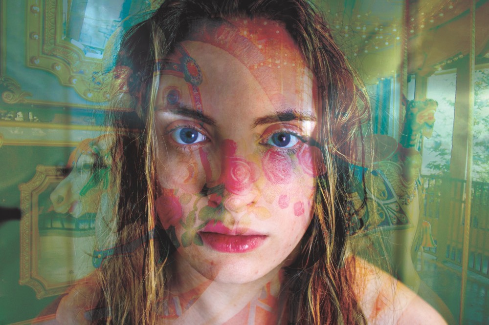 Psychedelic double exposure of a young woman's face looking straight at the camera through a hazy pattern.
